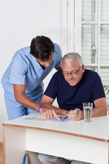 Healthcare professional in scrubs assisting an elderly man with paperwork in a bright room