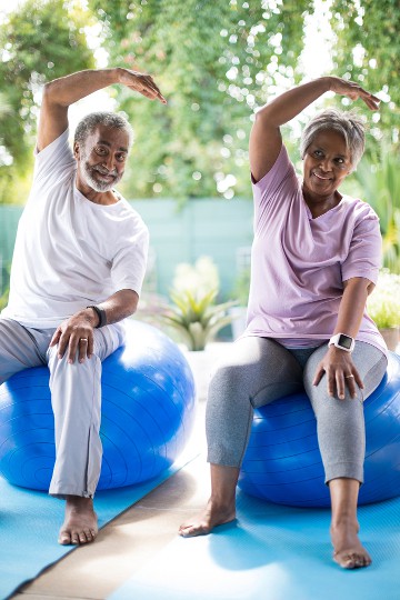 Senior couple doing stretching exercises on balance balls in a garden setting