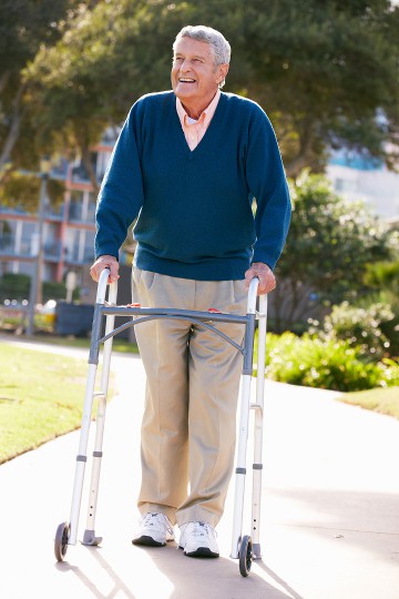 Elderly man smiling and walking with a walker in a sunny park setting