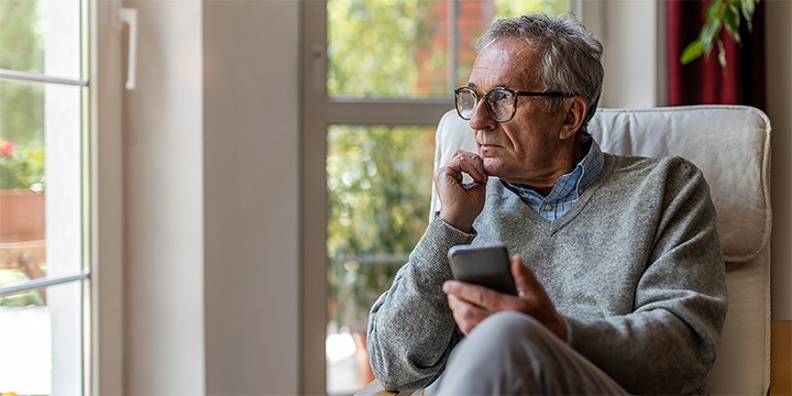 Elderly man sitting in a chair while holding his cell phone looking out the window