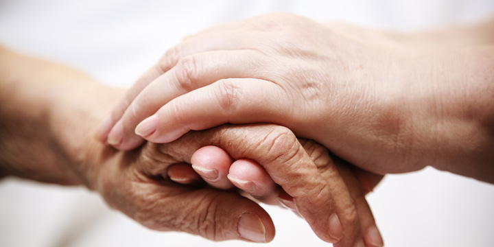 An older person's hand being held by the two hands of someone younger