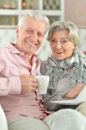 Smiling elderly couple relaxing on the couch with a cup of coffee and a magazine.