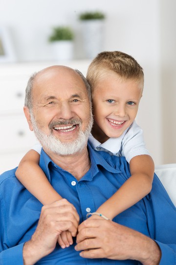 Smiling grandfather with white beard hugging young grandson in blue shirt