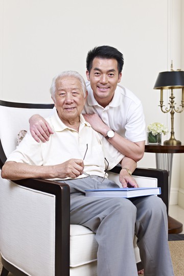 Elderly man and adult son smiling together on a couch with book and pen in a cozy living room setting