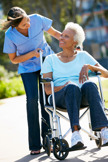 Older woman in a wheelchair looking over her shoulder to smile at a woman in medical scrubs who is pushing the wheelchair