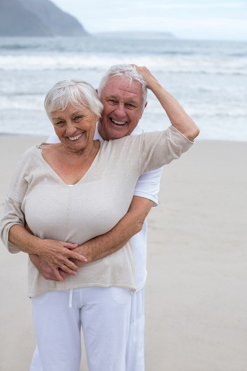 Happy elderly couple embracing on a cloudy beach with gentle smiles
