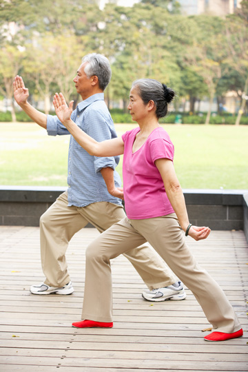 Older man and woman practicing tai chi, each with one foot forward under a bent front knee and one arm raised at an angle