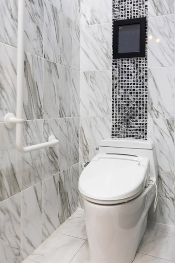 A closed toilet next to a grab bar in a bathroom with black and white marble tiles
