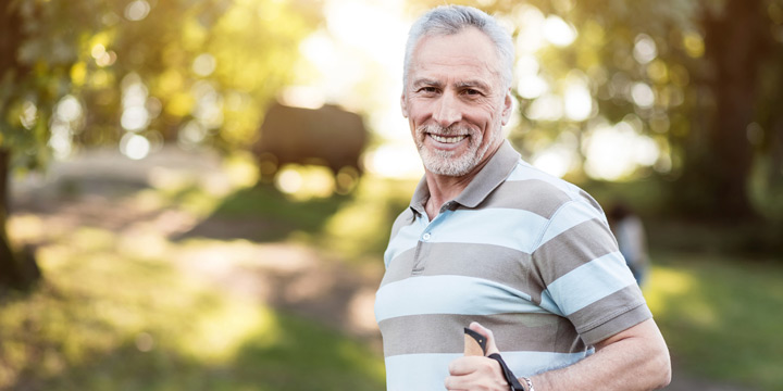 Elderly man wearing a striped t-shirt smiling on a sunny hiking trail