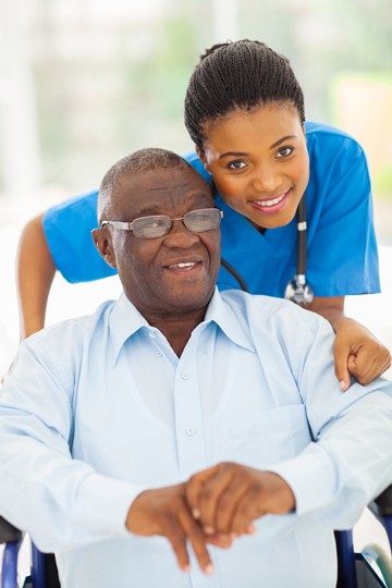 Elderly man smiling at a female nurse as they hold hands in a garden setting.