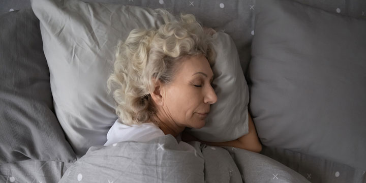 Woman with gray curly hair asleep in a bed