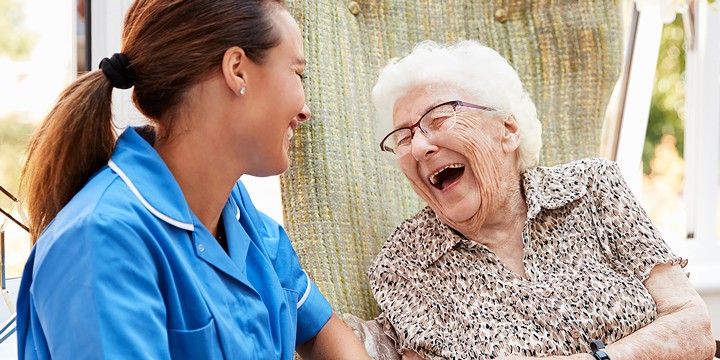 Senior woman sitting and laughing with assisted living care aid.