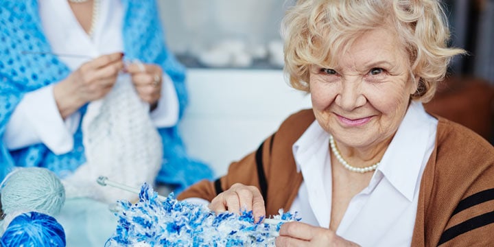 Smiling senior woman knitting using blue yarn