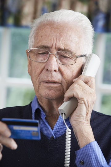 Elderly man holding a credit card and speaking on the telephone, potentially dealing with a financial issue