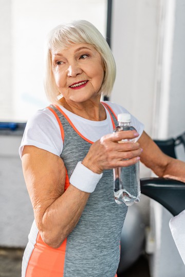 Elderly woman smiling and holding a water bottle in a gym setting
