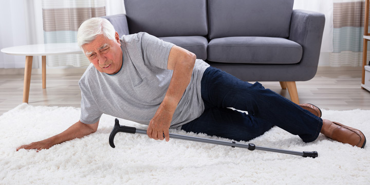 Elderly man falls onto white carpet holding his cane