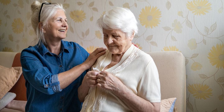 Senior women sitting on a couch while one buttons up a yellow cardigan