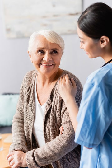 Smiling elderly woman being comforted by a female nurse in a blue uniform