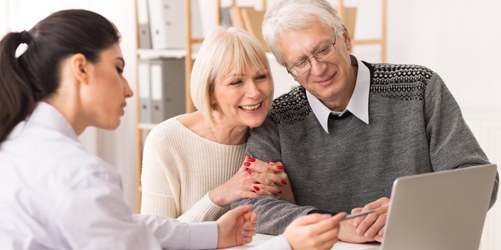 Smiling older couple sitting at a table with a young woman who is pointing to the screen of an open laptop they're looking at