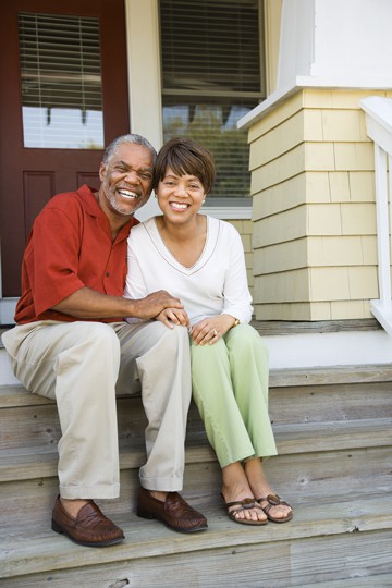 Smiling older couple sitting together on front porch steps of their home.