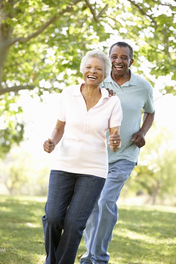 Smiling older man with his hand on shoulder of a smiling woman as they walk briskly on a sunny day with trees in background