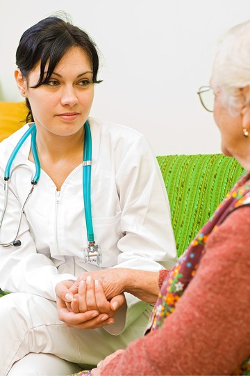 A nurse demonstrates empathy by holding the hand of an elderly woman in an assisted living community.