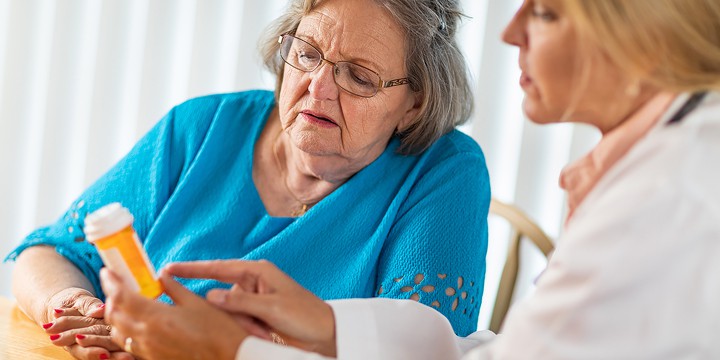 In an assisted living community, a female doctor reads the prescription label for pain medication to a worried senior patient