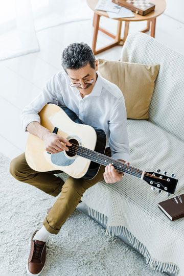 Man sitting on a sofa playing an acoustic guitar in a home setting