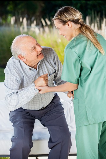 Elderly man with caregiver smiling and holding hands outdoors