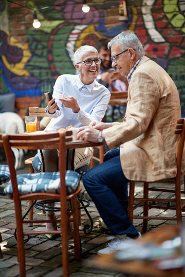 Older couple on a date engaging in a happy conversation at an outdoor cafe with colorful graffiti in the background.