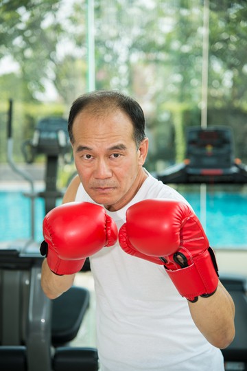 Mature man in a gym with red boxing gloves posing in front of exercise equipment and a pool.