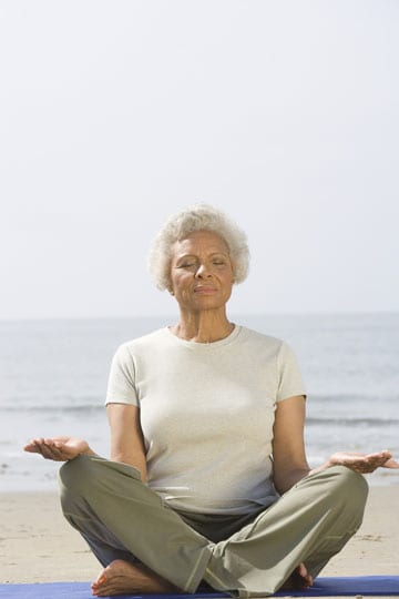 Older woman meditating on a mat at the beach