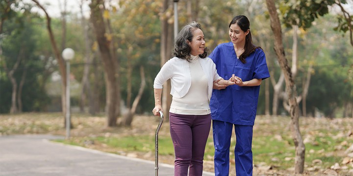A rehab nurse guides an elderly patient in the safe and effective use of her cane outdoors.
