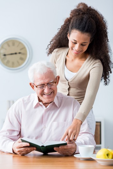 Young woman and older man smiling and looking at a book together