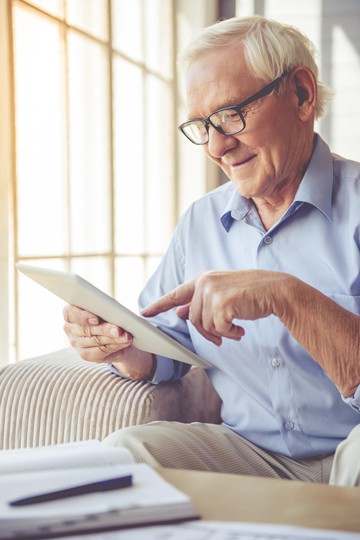 Elderly man with glasses smiling while using a tablet at home