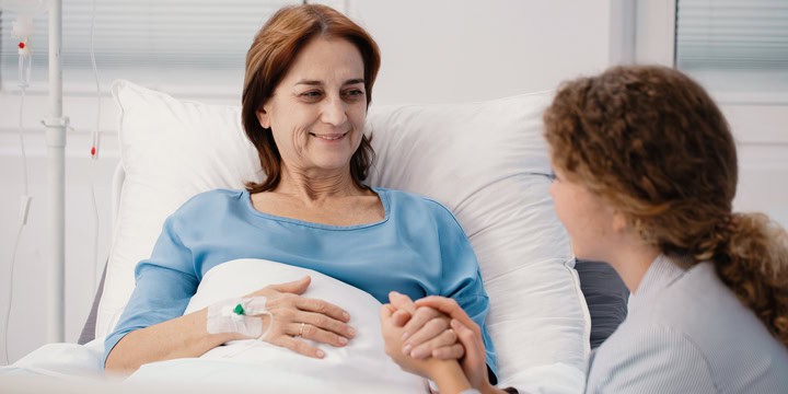 Smiling older woman receiving an IV in a hospital bed while holding hands with a young woman sitting beside her