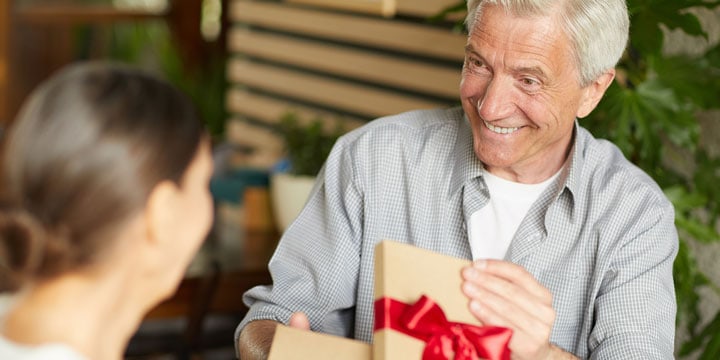 Senior man opening a gift box with a red bow from a family member