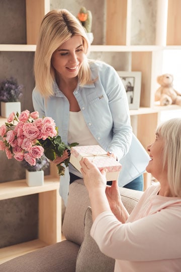 Young woman giving a Valentines gift an da  bouquet of pink roses to an older woman