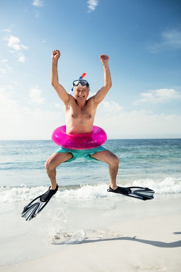 Man in snorkeling gear jumping with a pink inflatable ring on a beach