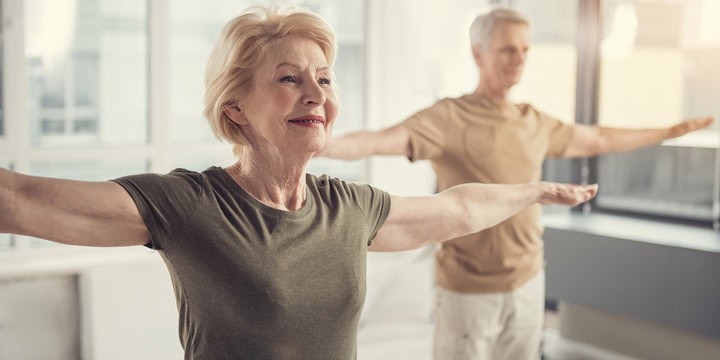 Man and woman standing with their arms stretched out to their sides in a room lined with windows