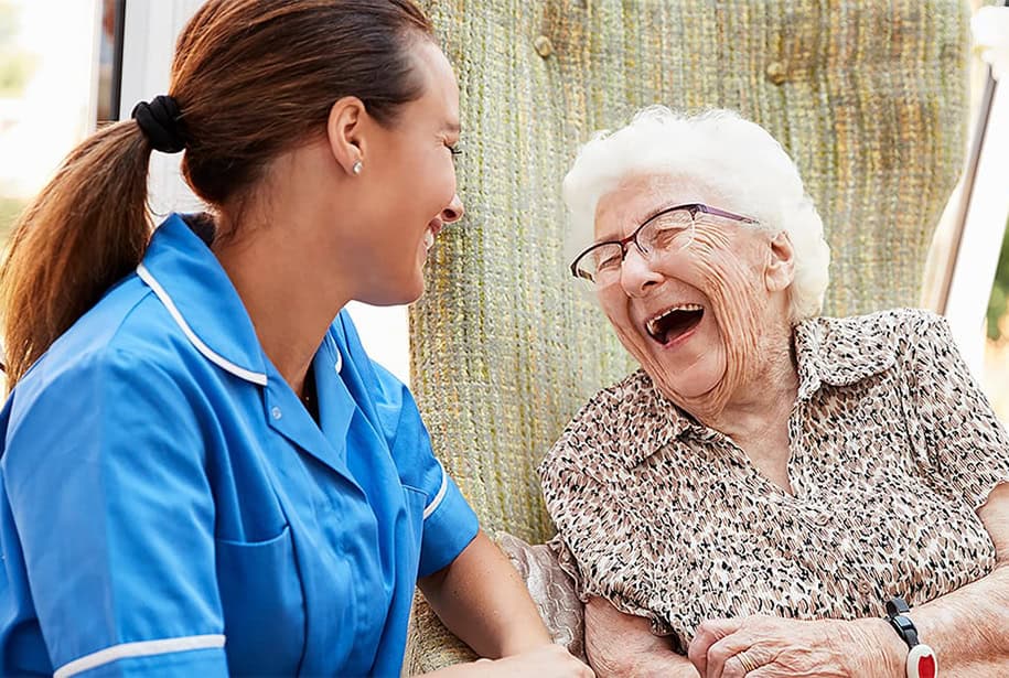 Senior woman sitting and laughing with assisted living care aid.