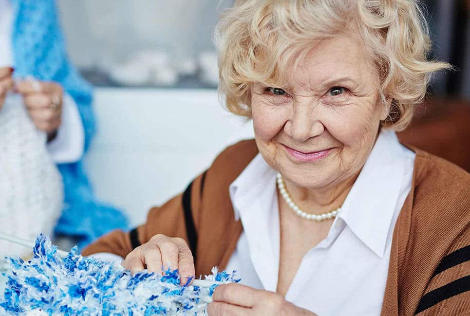 Smiling senior woman knitting using blue yarn