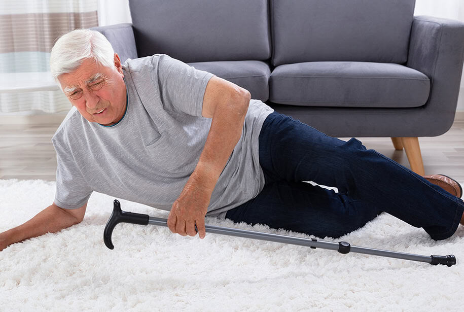 Elderly man falls onto white carpet holding his cane