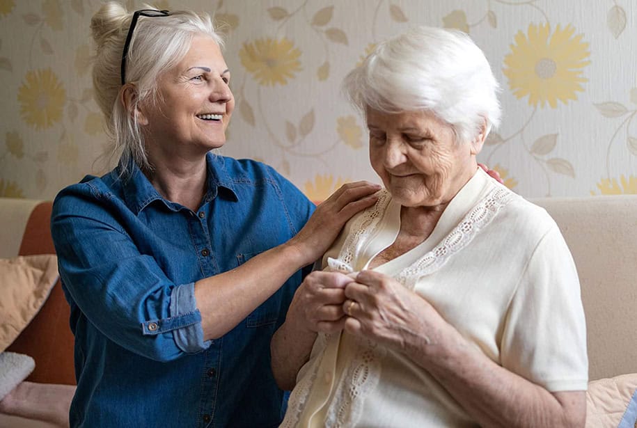 Senior women sitting on a couch while one buttons up a yellow cardigan