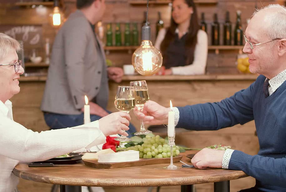 Senior couple toasting with wine at a cozy restaurant with candlelight and a cheese platter.