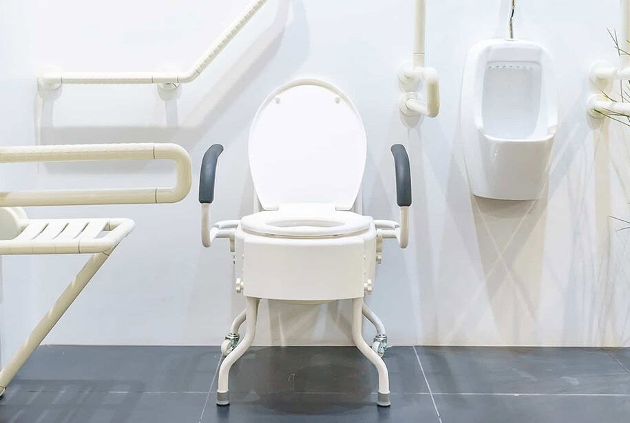 A commode and a urinal surrounded by various grab bars in a white-walled room