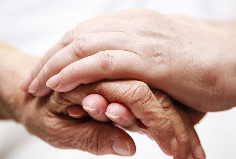 An older person's hand being held by the two hands of someone younger