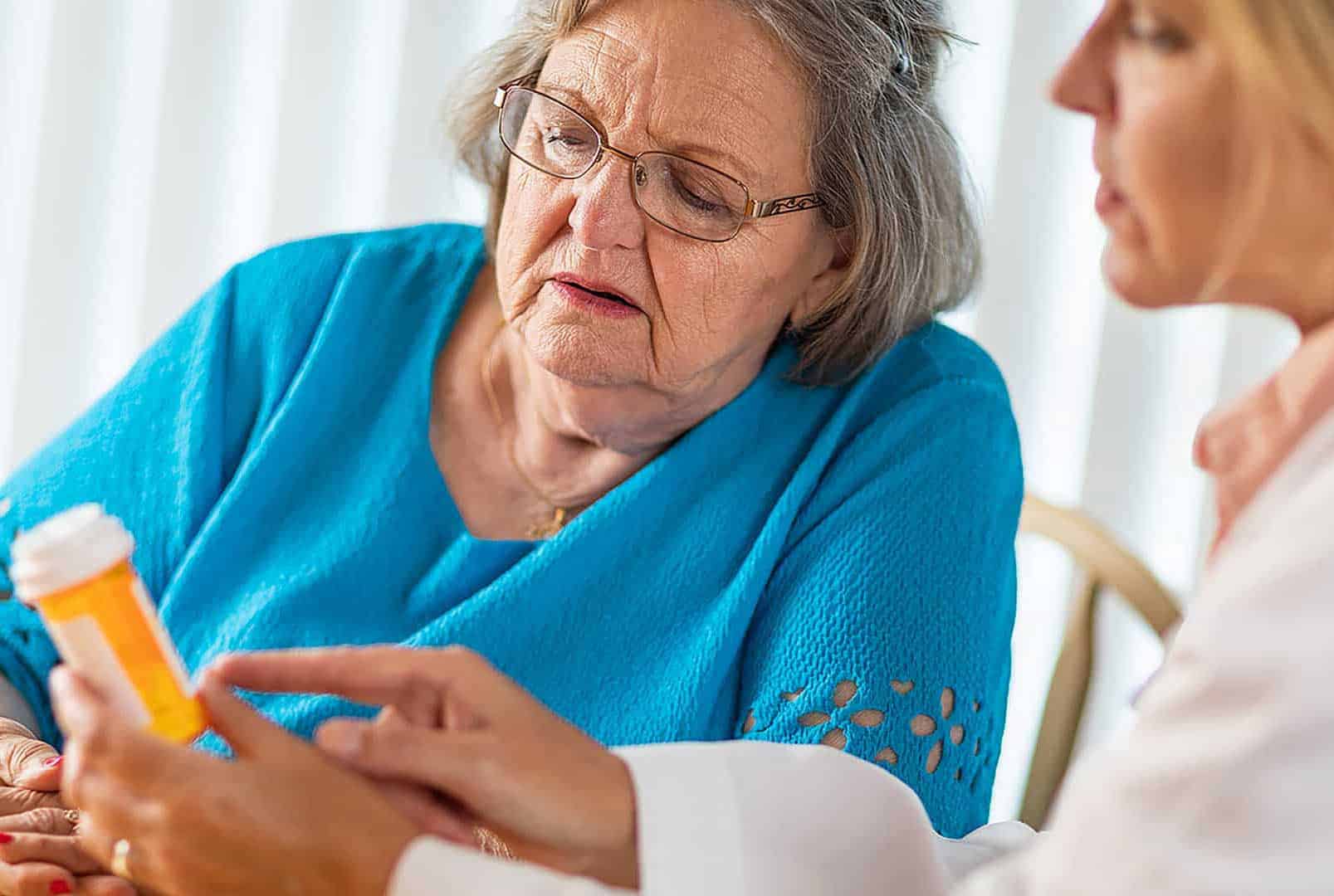 In an assisted living community, a female doctor reads the prescription label for pain medication to a worried senior patient
