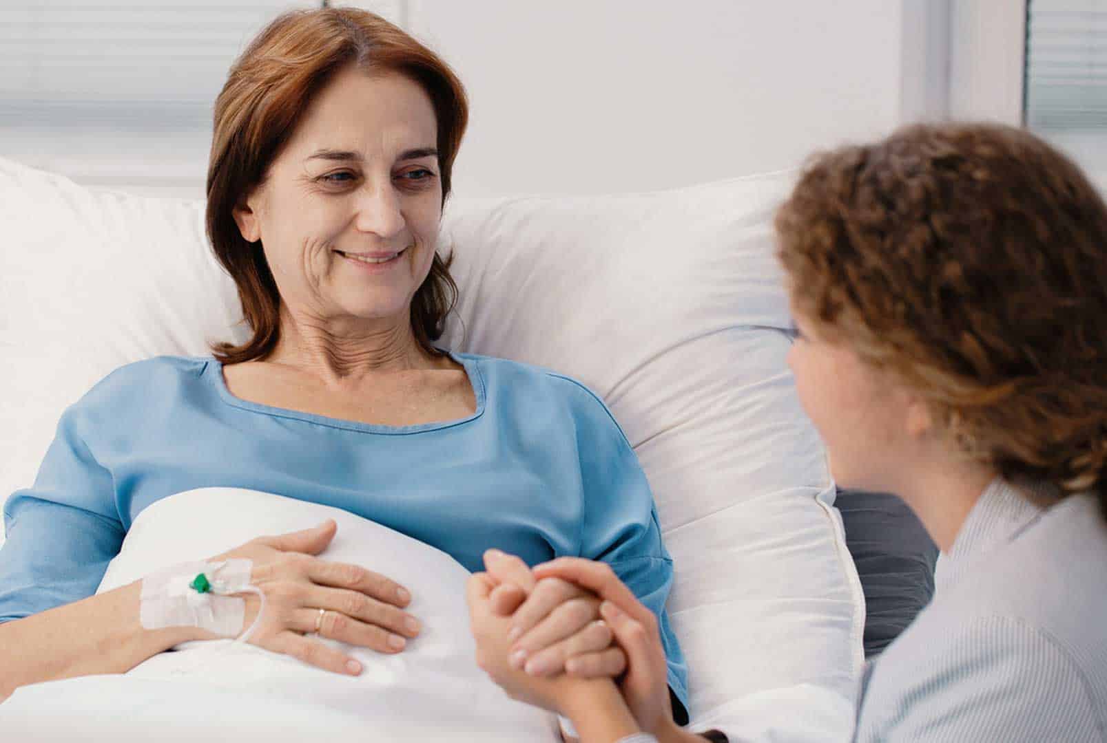 Smiling older woman receiving an IV in a hospital bed while holding hands with a young woman sitting beside her
